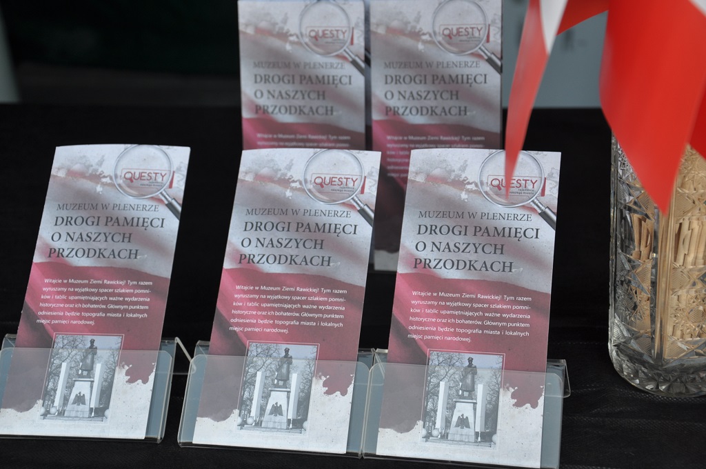  W ramach tegorocznych lokalnych obchodów Narodowego Święta Niepodległości Muzeum Ziemi Rawickiej zaprosiło mieszkańców oraz turystów odwiedzających Rawicz do udziału w specjalnym wydarzeniu kulturalno-edukacyjnym. 11 listopada odbyła się premiera kolejnego muzealnego questu pt. „Drogi pamięci o naszych przodkach”.  Na czynnym w tym dniu muzealnym stoisku promocyjnym uczestnicy zabawy otrzymywali karty zadań z opisem „szlaku rawickich miejsc pamięci narodowej” oraz zagadkami, których rozwiązanie było możliwe tylko w ramach przejścia całej trasy i obejrzenia wskazanych w treści questu obiektów historycznych. Stoisko zostało zaaranżowane tematycznie – przed ratuszem stanęła budka polskiego strażnika oraz szlaban graniczny, przypominające o tym, że po odzyskaniu niepodległości zaledwie kilka kilometrów od Rawicza była wytyczona polsko-niemiecka granica państwowa. Na zwiedzających w muzeum czekał wyjątkowy przewodnik – sam marszałek Piłsudski w galowym mundurze. W rolę bohatera narodowego wcielił się jeden z pracowników muzeum.  Na „szlak miejsc pamięci” wyruszyło kilkadziesiąt osób, zarówno pieszo, jak i rowerami. Ponad dwadzieścia drużyn rodzinnych prawidłowo rozwiązało questowe hasło, otrzymując na zakończenie muzealną pieczęć oraz upominki związane z obchodami Święta Niepodległości. Rodziny z dziećmi spotkały się także w ratuszu na międzypokoleniowych muzealnych warsztatach manualnych, których tematem również były barwy i symbole narodowe. Uczestnicy warsztatów wykonywali tym razem ekologiczne przestrzenne mapy Polski. 